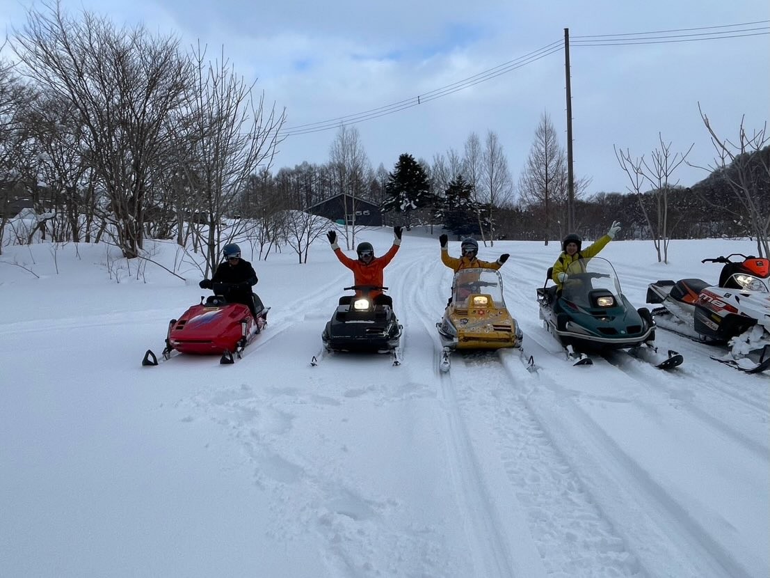 Five snowmobiles lined up on the snowfield, riders waving