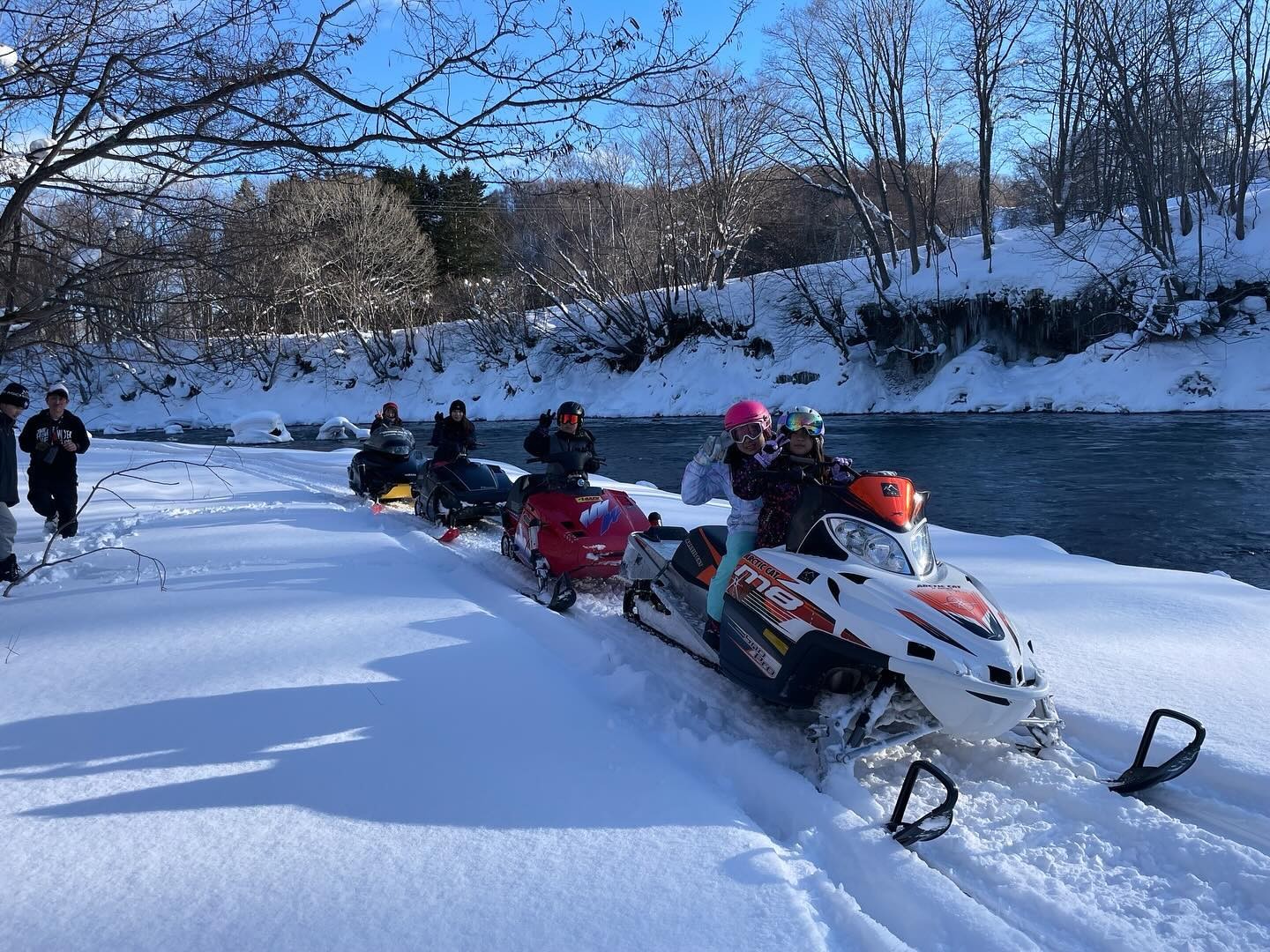 Snowmobiles and riders along the river